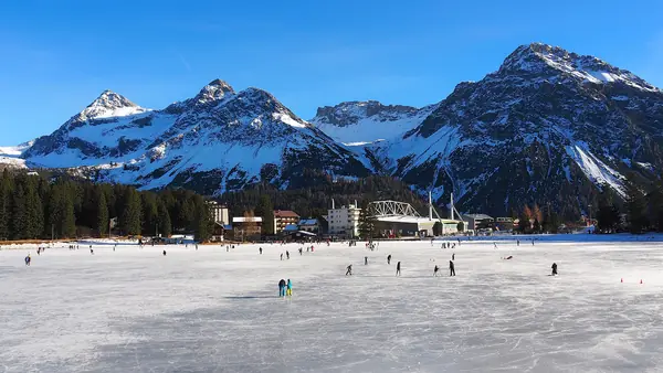Patinage sur le lac Obersee gelé, village d'Arosa et montagnes enneigées, décembre