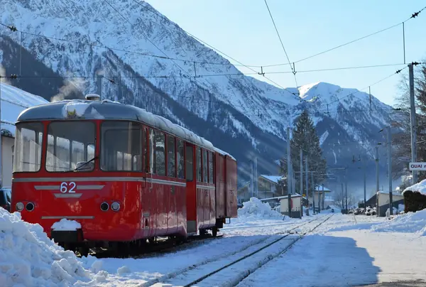 Un train rouge à l'arrêt dans une gare enneigée de la vallée de Chamonix