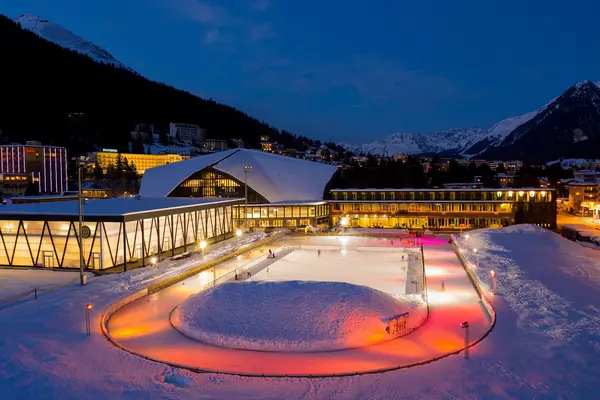 Patinoire Eistraum de Davos éclairée à la tombée de la nuit, ville enneigée