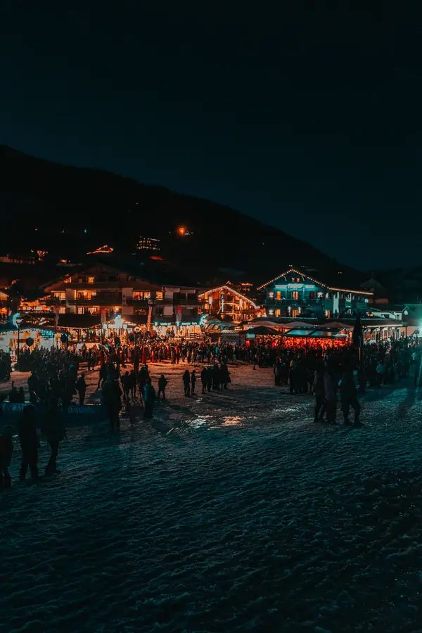 Front de neige des Gets la nuit, chalets éclairés et foule en plan large