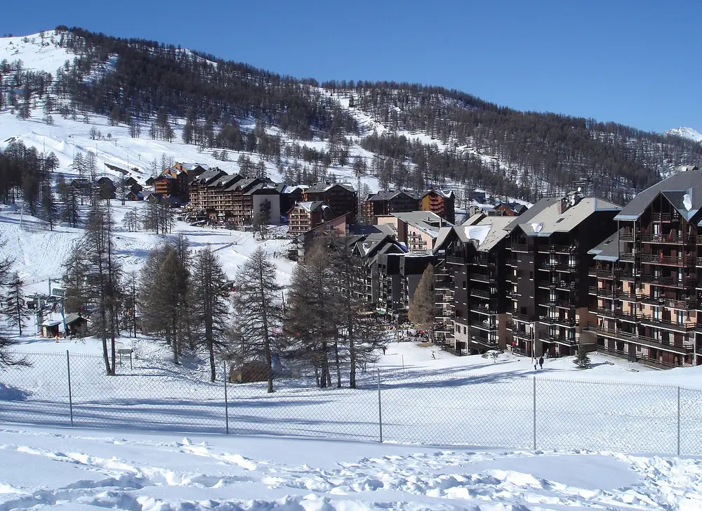 Les immeubles de Risoul 1850 en lisière de mélèzes, pistes enneigées au-dessus (février 2006)