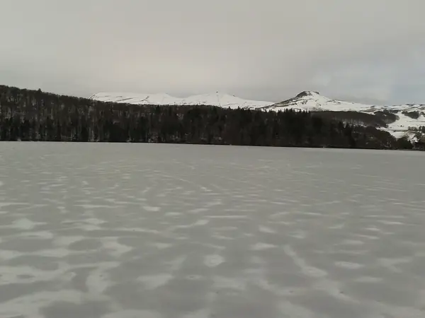 Lac Pavin gelé, avec la station de Super-Besse et les sommets enneigés à l'arrière-plan, mars 2018