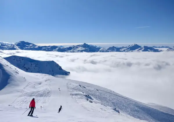 Skieurs sur une piste de Val Thorens au-dessus d'une mer de nuages